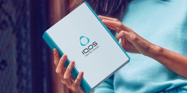 Eine Frau öffnet eine IQOS Box, die ihr nach Hause geliefert wurde.