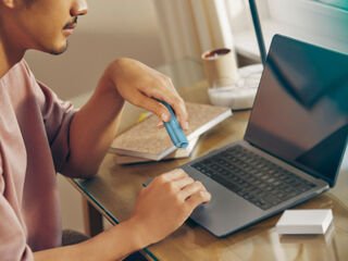 Hands typing on laptop while holding IQOS Originals ONE heated tobacco device.