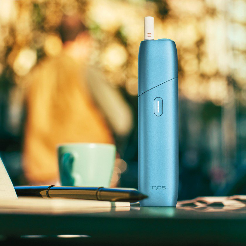 Blue IQOS Originals ONE device with HEETS stick next to coffee cup.