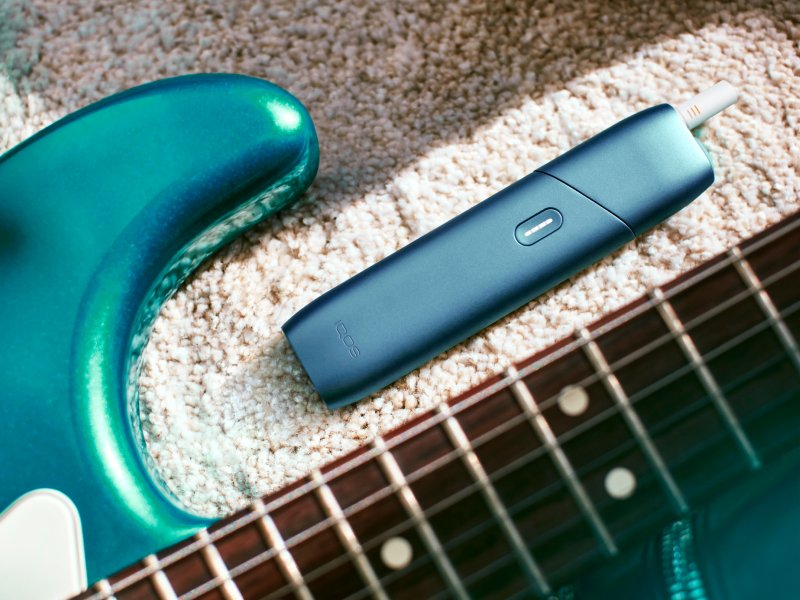 IQOS Originals One heated tobacco device, next to a turquoise guitar.
