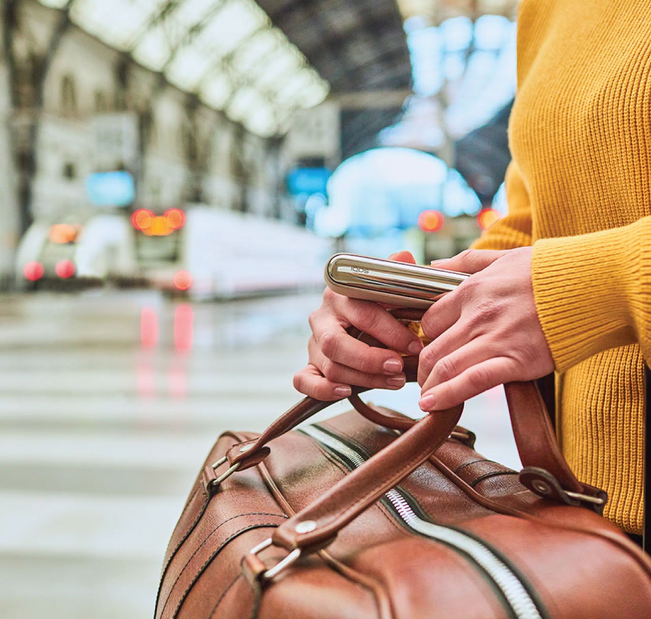 Travel documents, a mobile phone and an IQOS ILUMA PRIME Holder and Pocket Charger on a table.