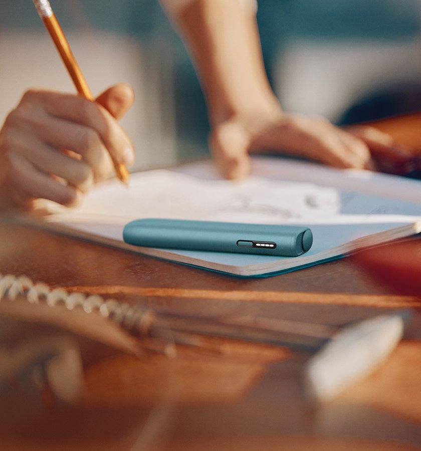 IQOS ILUMA i ONE color Breeze Blue encima de un cuaderno