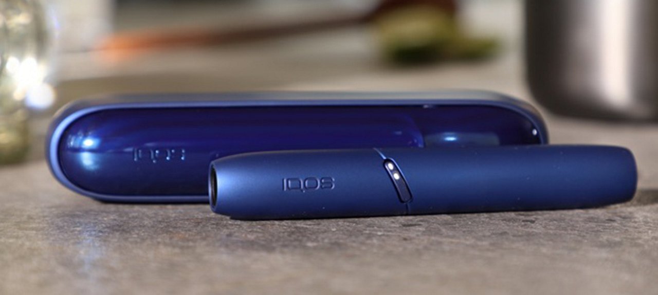 A blue IQOS and its cover lying on a table