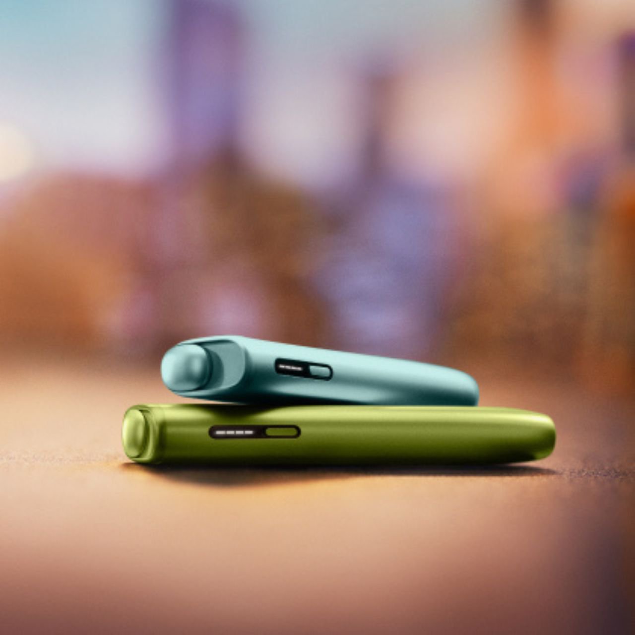 deux iqos iluma i one couleur aigue-marine et vert anis sur fond boisé.