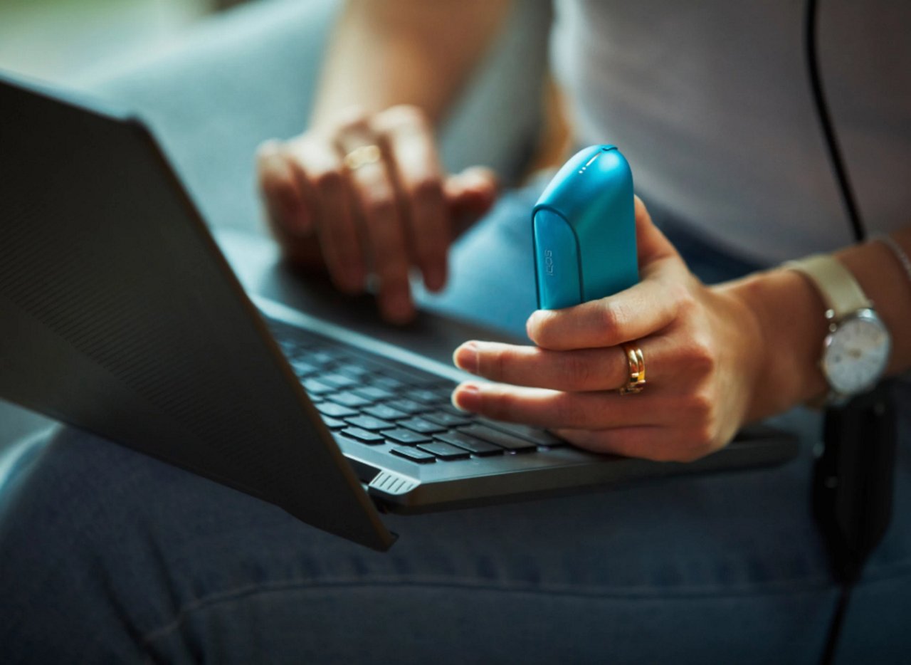 Žena píše na notebooku a drží v ruce IQOS zařízení