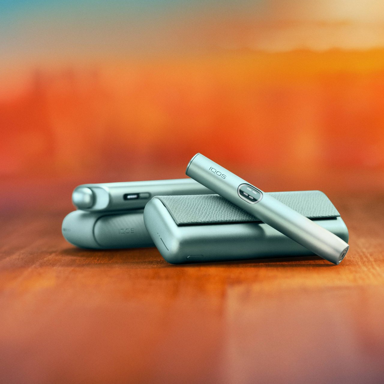IQOS ILUMA i devices on wooden surface, featuring holder and charger against a blurred orange background.