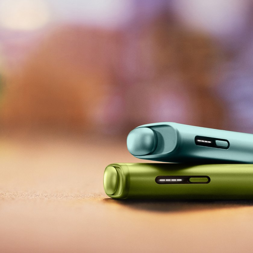 A Breeze Blue IQOS ILUMA i ONE device on top of a Leafy Green IQOS ILUMA i ONE device.