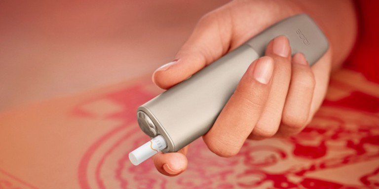 A woman holding an IQOS device looking at a laptop.