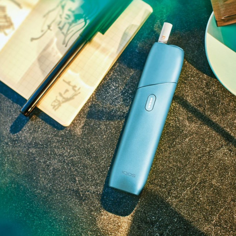 Turquoise IQOS Originals One heated tobacco device on a fabric table mat.