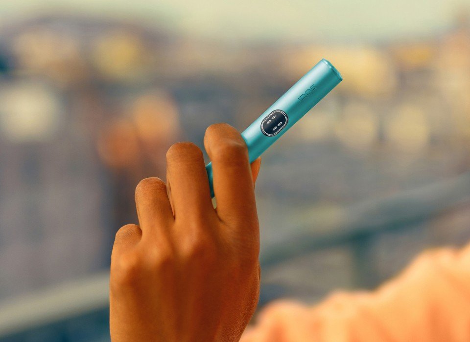 Hand holding a blue IQOS ILUMA i device.