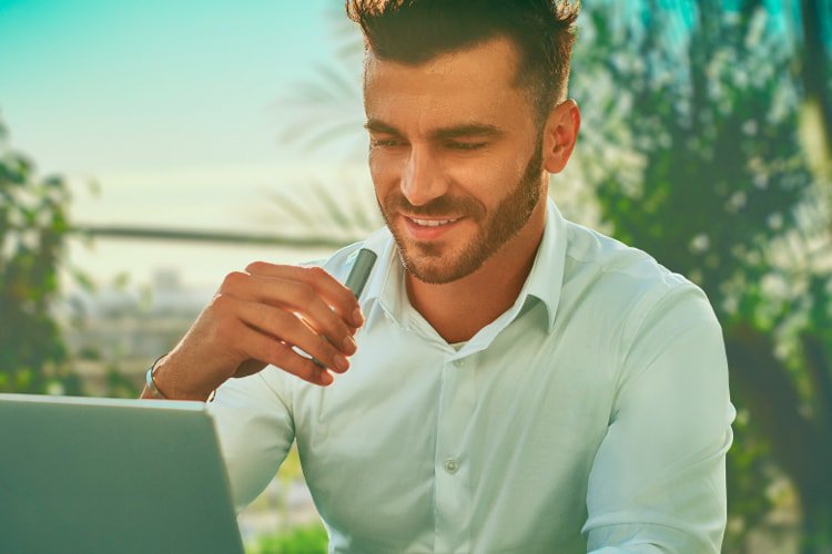 A man working on a laptop while holding an IQOS ILUMA device.