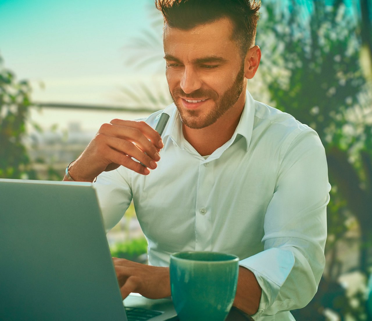 A man working on a laptop while holding an IQOS ILUMA device.