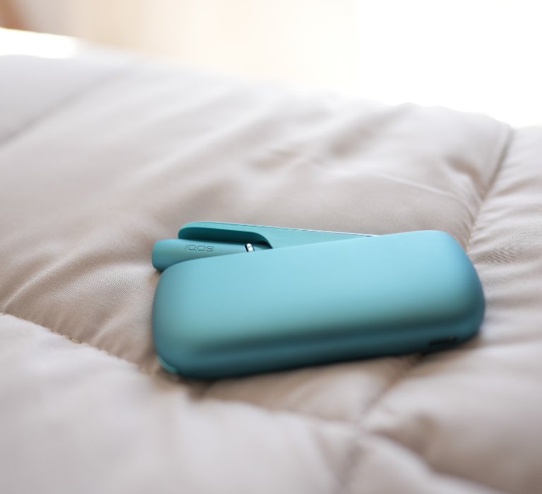 Turquoise IQOS Originals Duo device on a shiny coffee table.