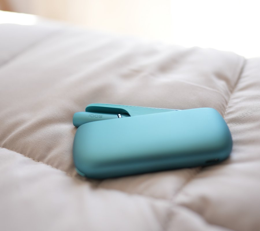 Turquoise IQOS Originals Duo device on a shiny coffee table.