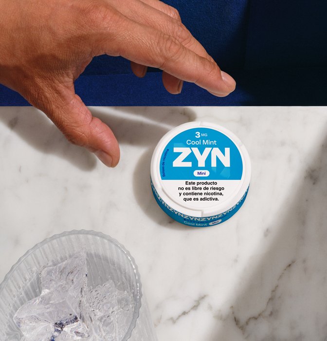 Mano agarrando una lata de Zyn Cool Mint de 3 mg sobre una mesa de marmol.