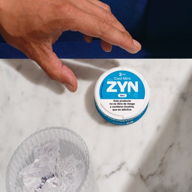 Mano agarrando una lata de Zyn Cool Mint de 3 mg sobre una mesa de marmol.