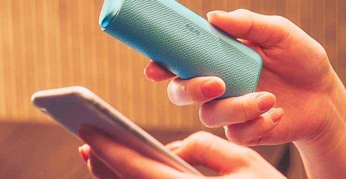 Person hält Smartphone und IQOS Kit in der Hand, Laptop im Hintergrund.
