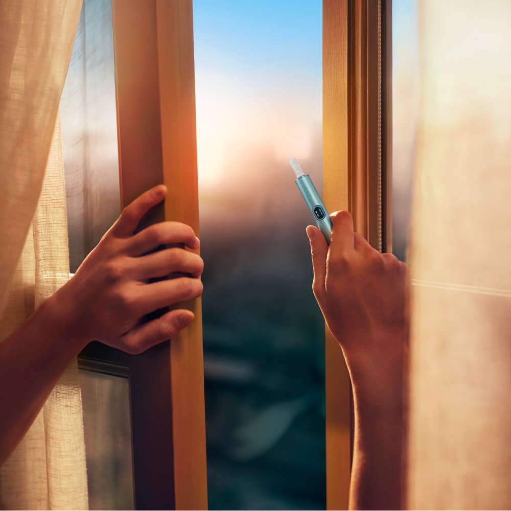 Hand hält IQOS ILUMA i am Fenster mit Blick nach draußen