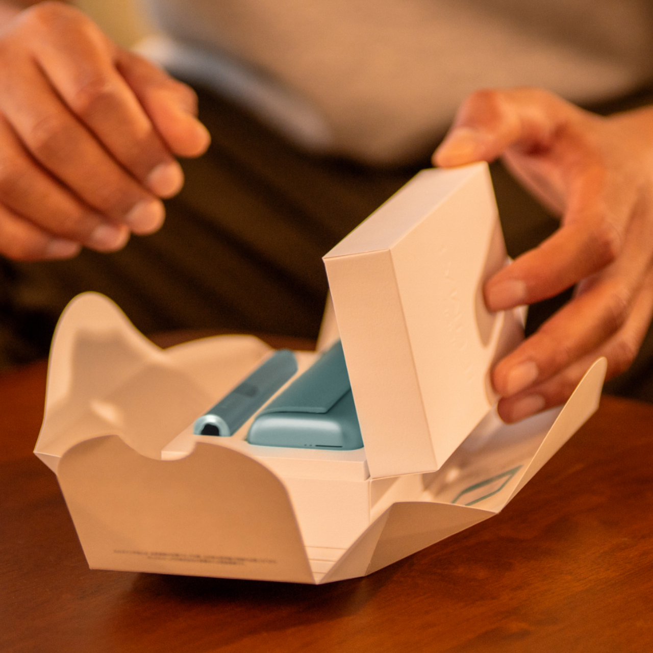 Person öffnet die Verpackung eines IQOS ILUMA i PRIME Gerätes