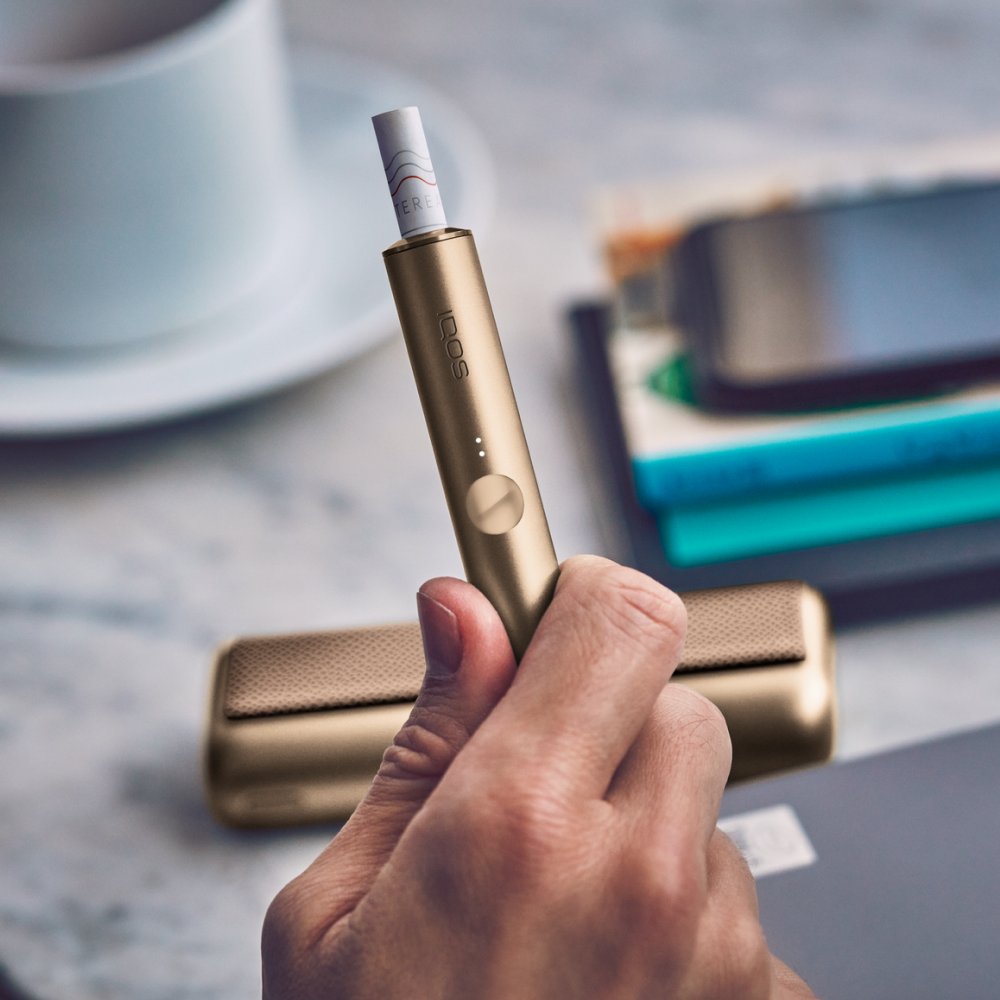 Hand hält einen IQOS ILUMA PRIME Holder neben einem Handy