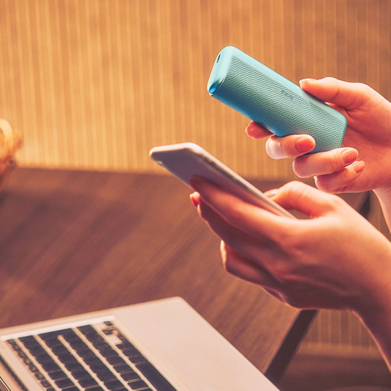 Person hält Smartphone und IQOS Kit in der Hand, Laptop im Hintergrund.
