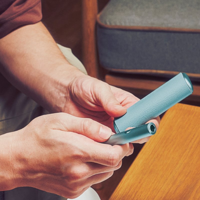 Person hält IQOS Tabakerhitzer und Kit in der Hand.