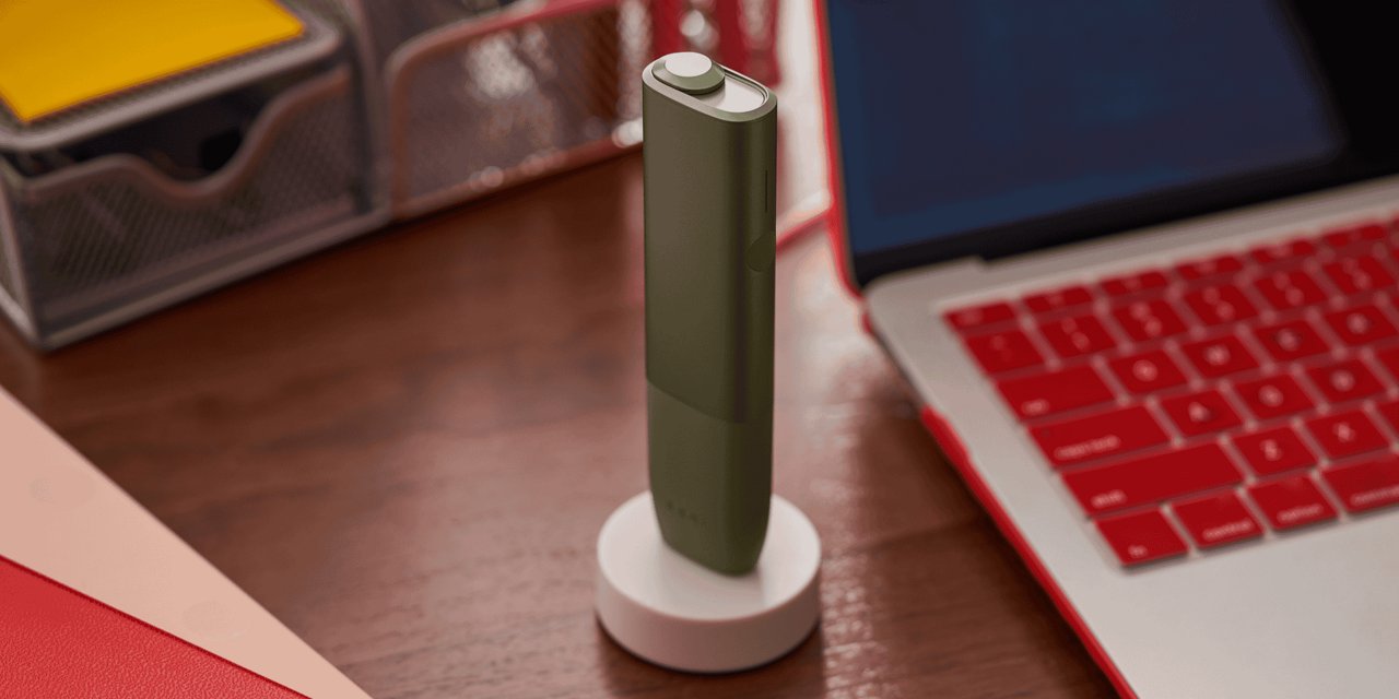 Ein IQOS ILUMA ONE Gerät neben einem Laptop in einer Ladestation.