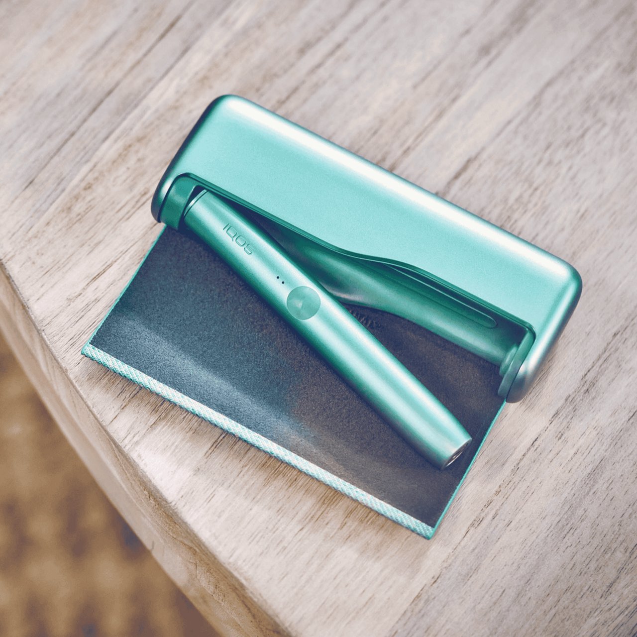 Ein jadegrünes IQOS ILUMA PRIME Gerät liegt auf einem Holztisch