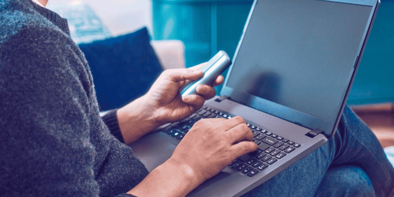 Ein Mann arbeitet an einem Laptop und hält ein IQOS ILUMA Gerät in der Hand.