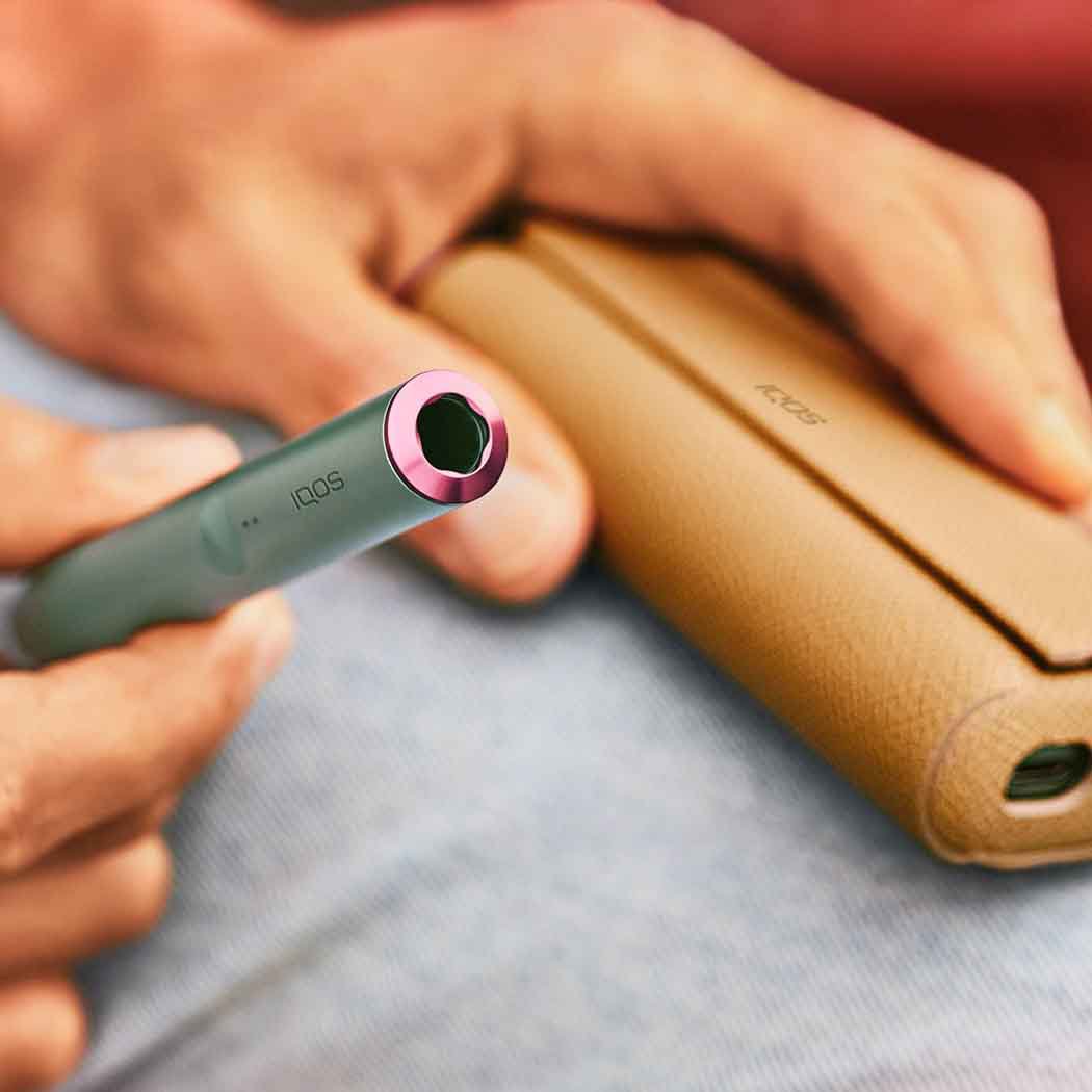 Pemegang IQOS ILUMA Jade Green dengan aksesori cincin yang dipegang oleh seseorang dengan balutan penuh kulit.