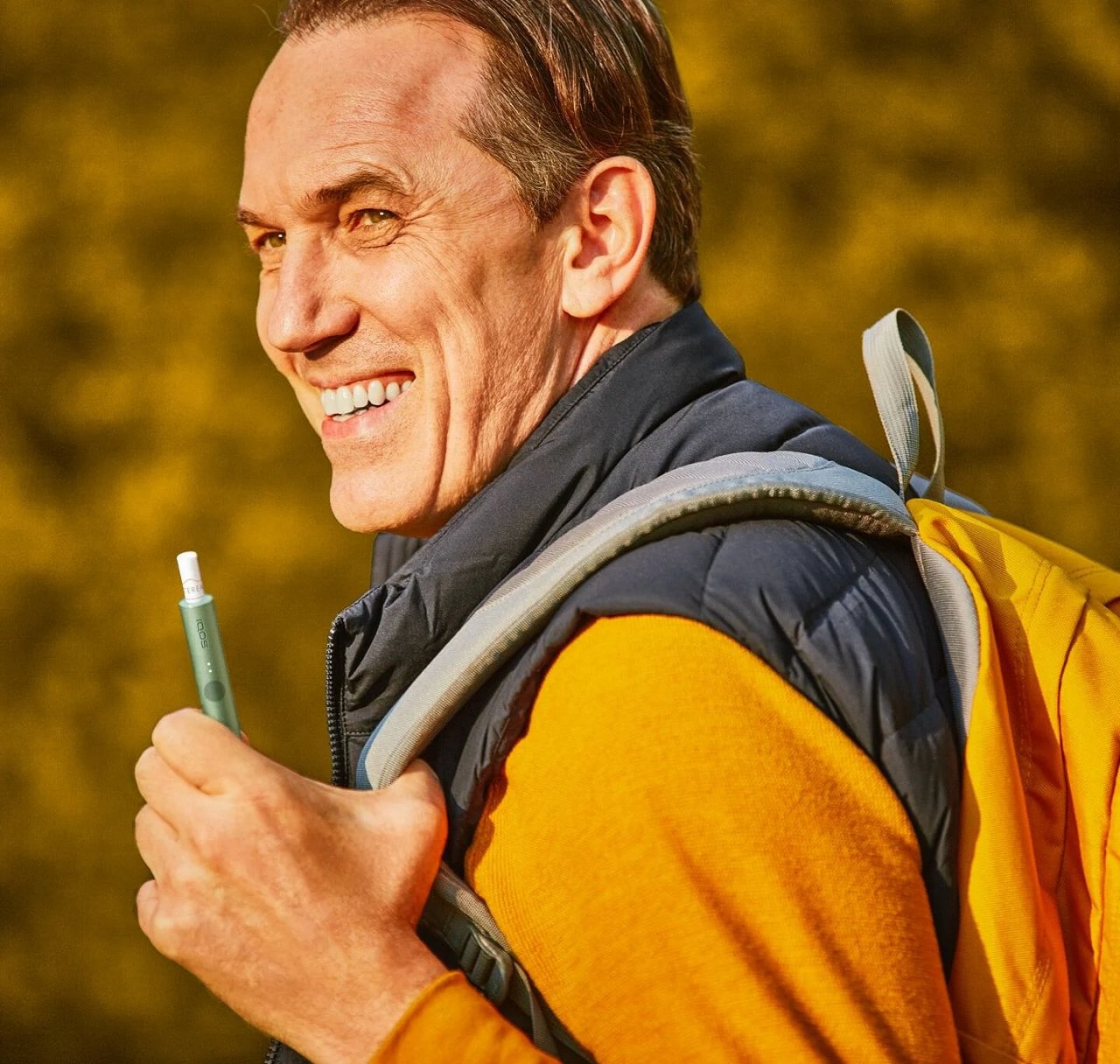 A man with a rucksack holds an IQOS device.