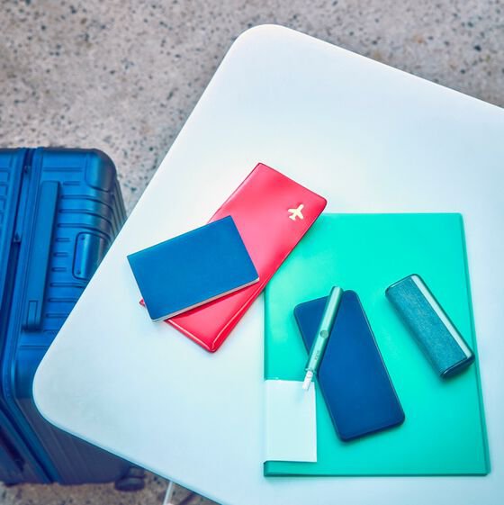 Travel documents, a mobile phone and an IQOS ILUMA PRIME Holder and Pocket Charger on a table.