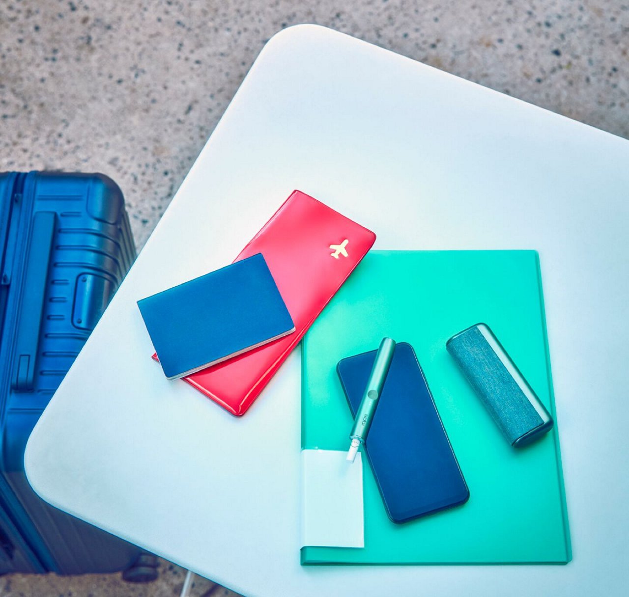 Travel documents, a mobile phone and an IQOS ILUMA PRIME Holder and Pocket Charger on a table.