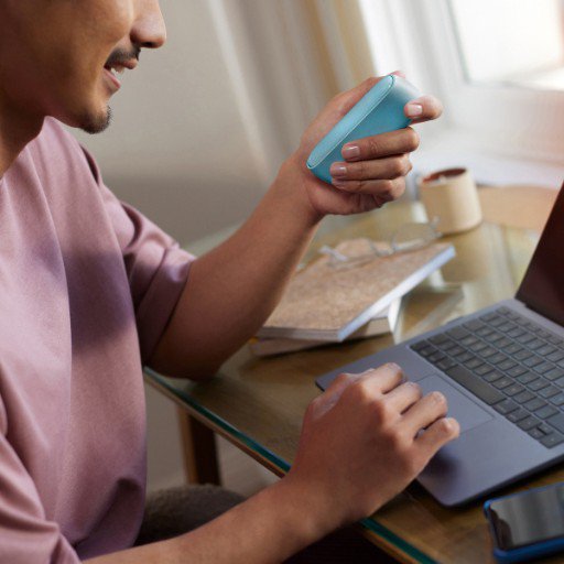 Man holding IQOS originals Duo device and typing on laptop.