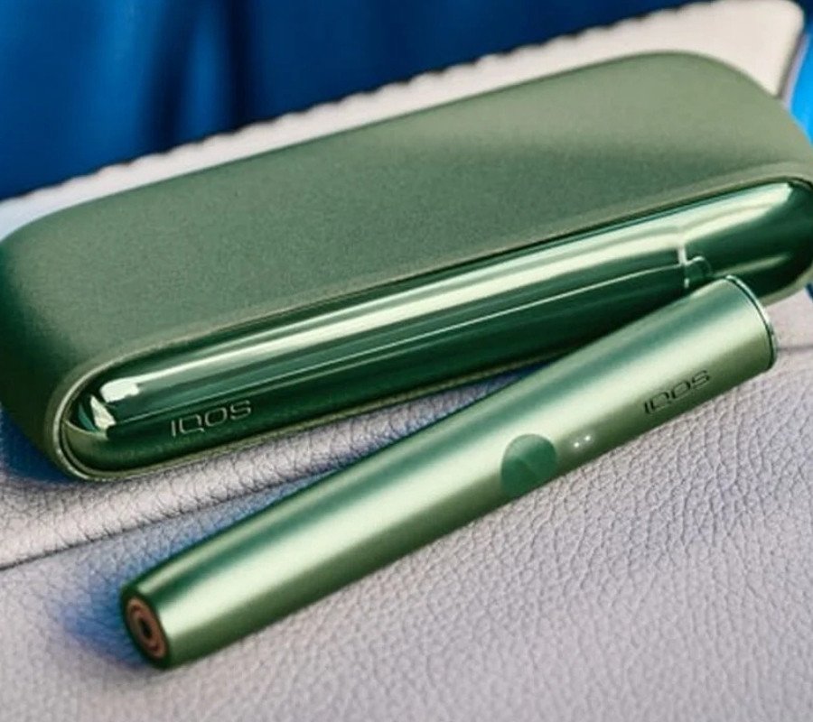 A woman holding an IQOS ILUMA device while looking at a laptop.