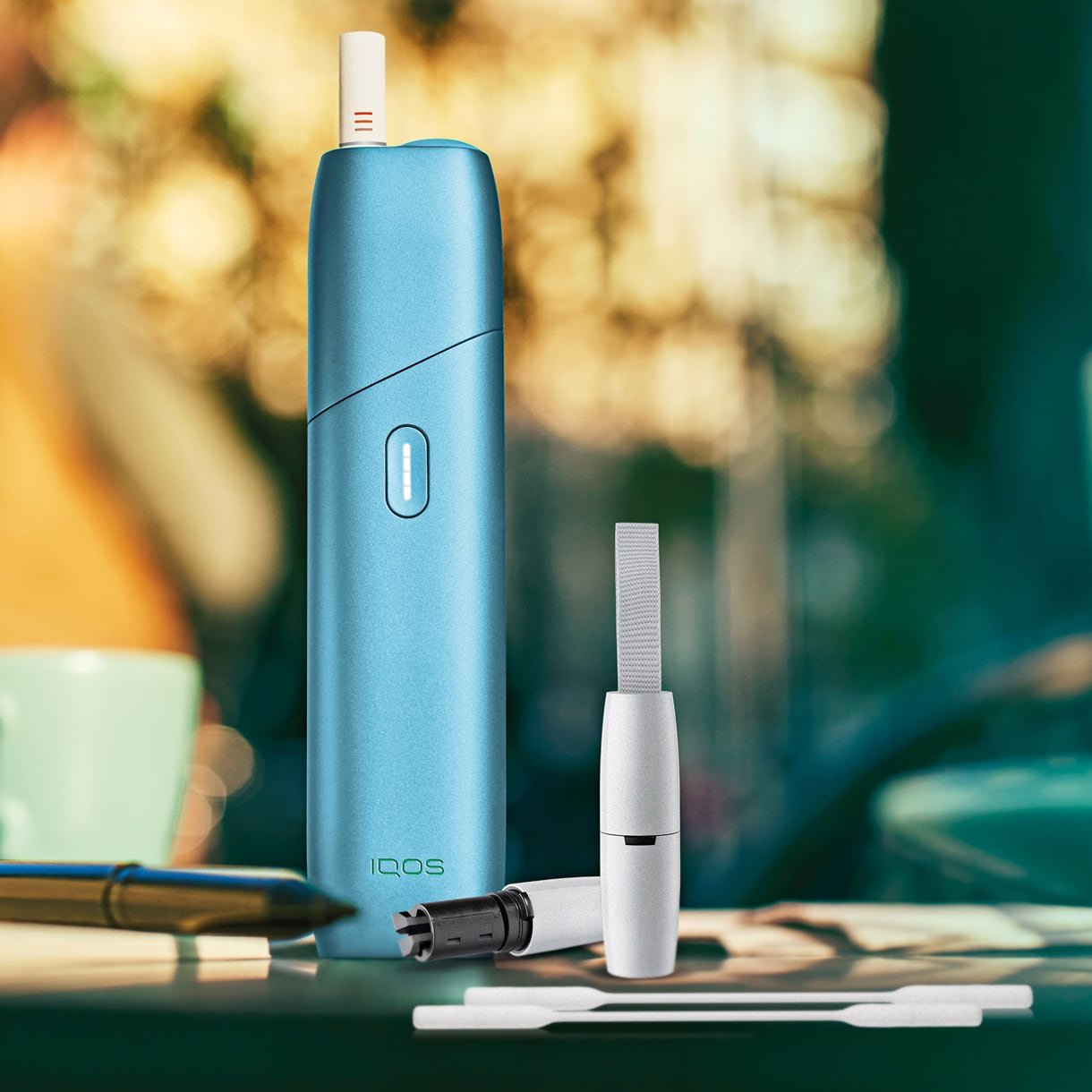 IQOS Originals ONE in türkis mit Reinigungszubehör auf einem Tisch