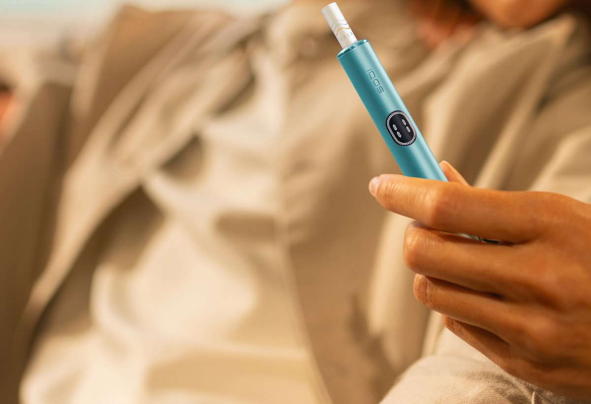 Person hält ein IQOS vor einem unscharfen Hintergrund.