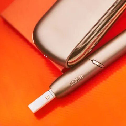 IQOS holder with HEETS stick next to a charger on red notebook
