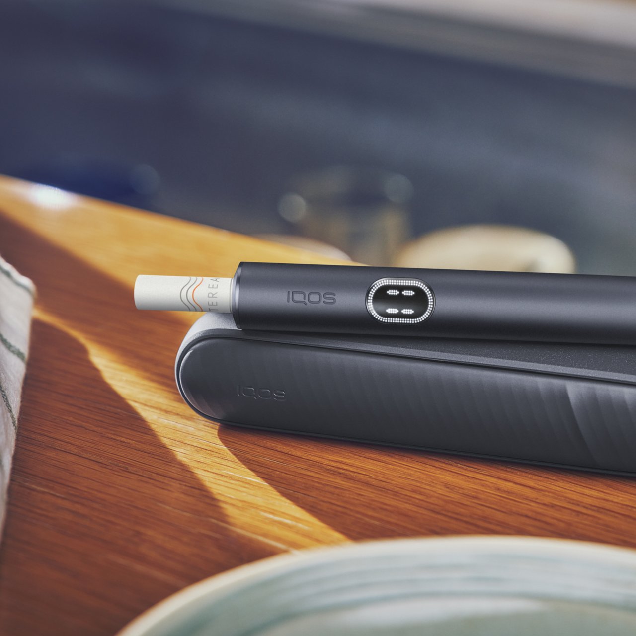 IQOS ILUMA i Tabakerhitzer liegend auf einem Holztisch.