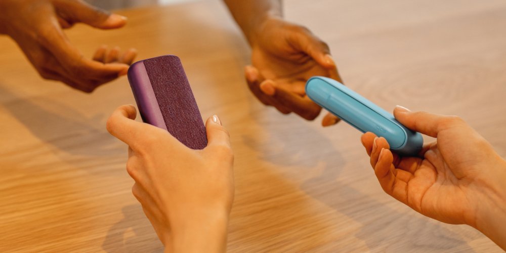 Zwei ILUMA i Tabakerhitzer werden zwischen zwei Personen übergeben