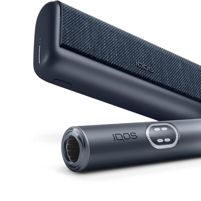 Ак фондо кара графит түсүндөгү IQOS ILUMA i PRIME кармагычы заряддагычтын алдында