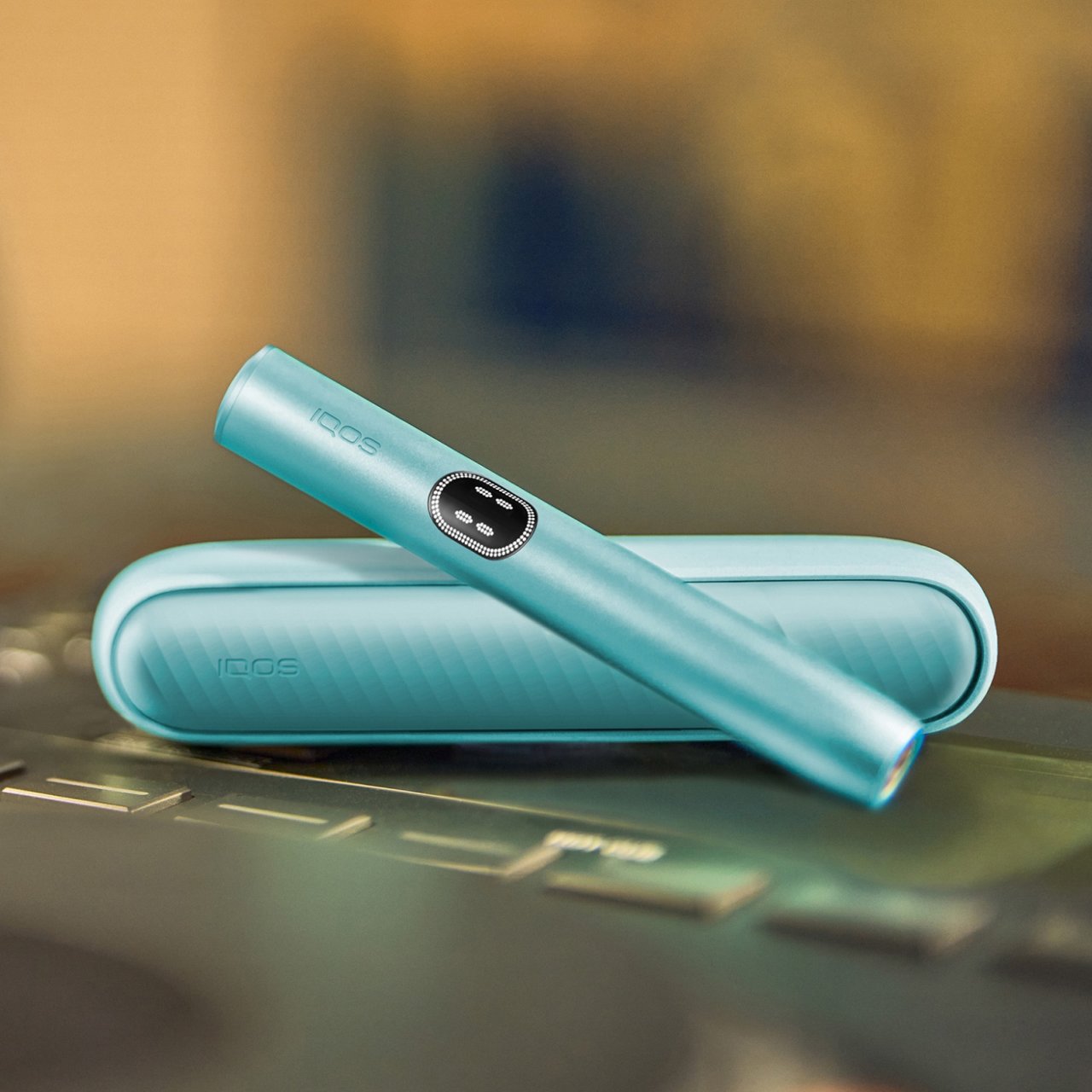 Устройство IQOS ILUMA i цвета Лазурный бриз над зарядным устройством на поверхности