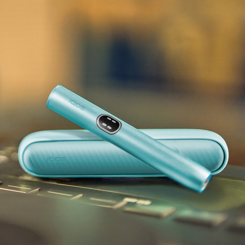 Устройство IQOS ILUMA i цвета Лазурный бриз над зарядным устройством на поверхности