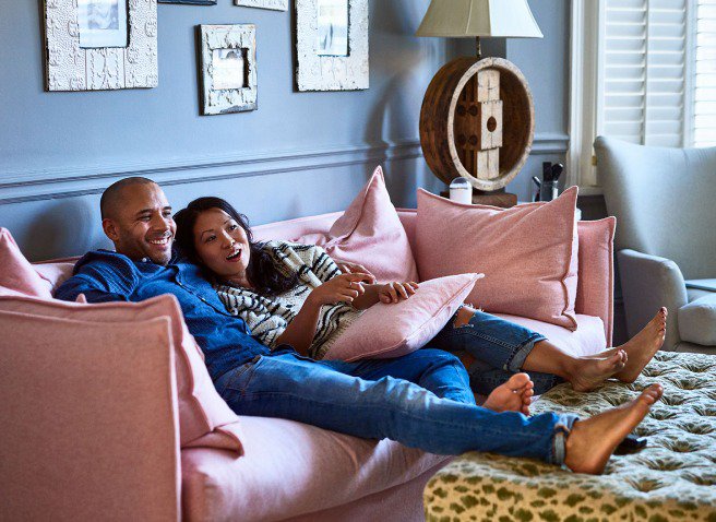 A man and a woman sitting on a pink couch in the living room