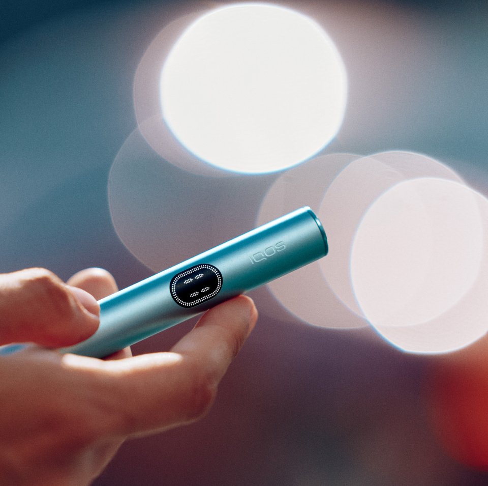 IQOS ILUMA i One color turquesa dentro de una bolsa verde en el asiento del auto.
