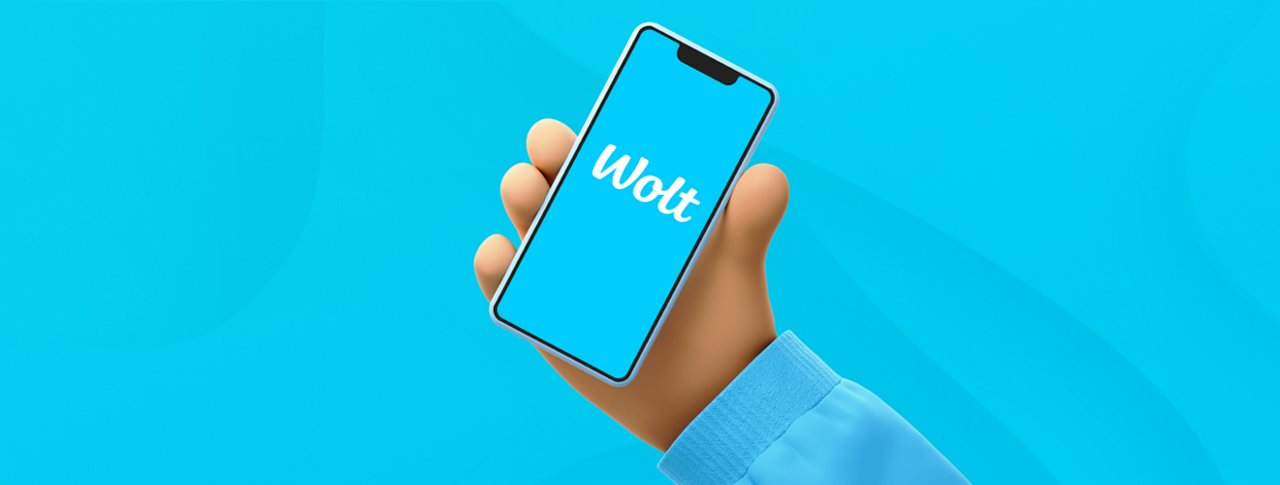 Ilustrace ruky držící mobilní telefon s aplikací Wolt na obrazovce na tyrkysovém pozadí.