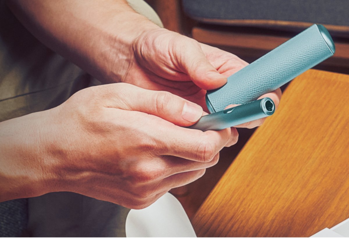 Hände halten ein IQOS ILUMA i.