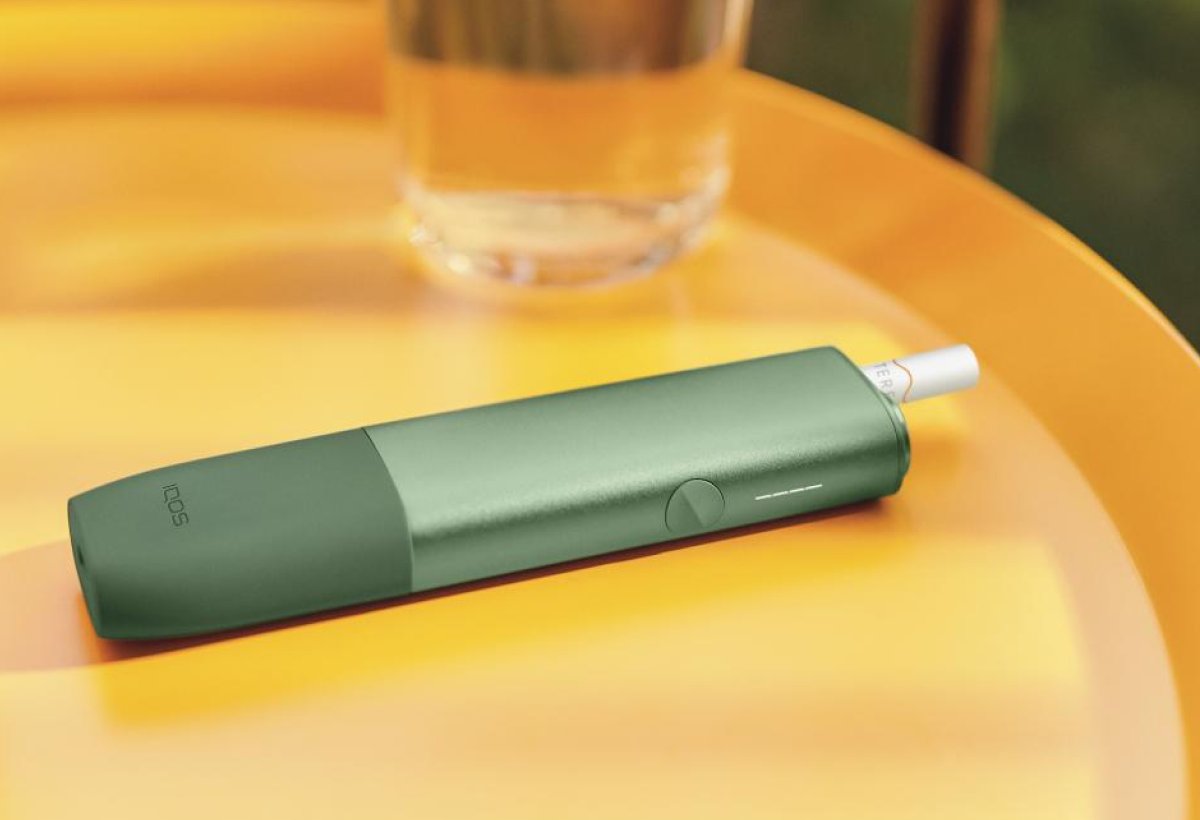 IQOS ILUMA One in grün auf einem gelben Tisch.