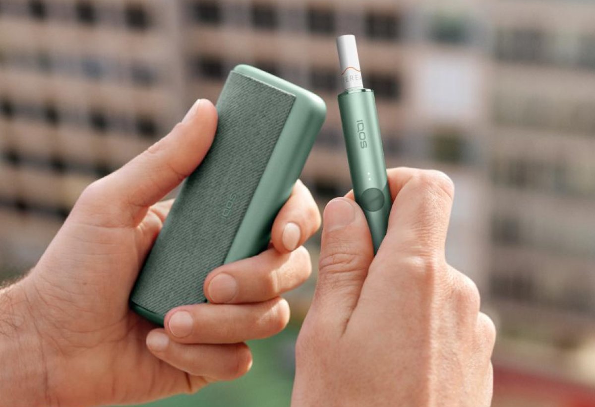 Eine Hand hält ein IQOS ILUMA PRIME Charger und einen Holder.