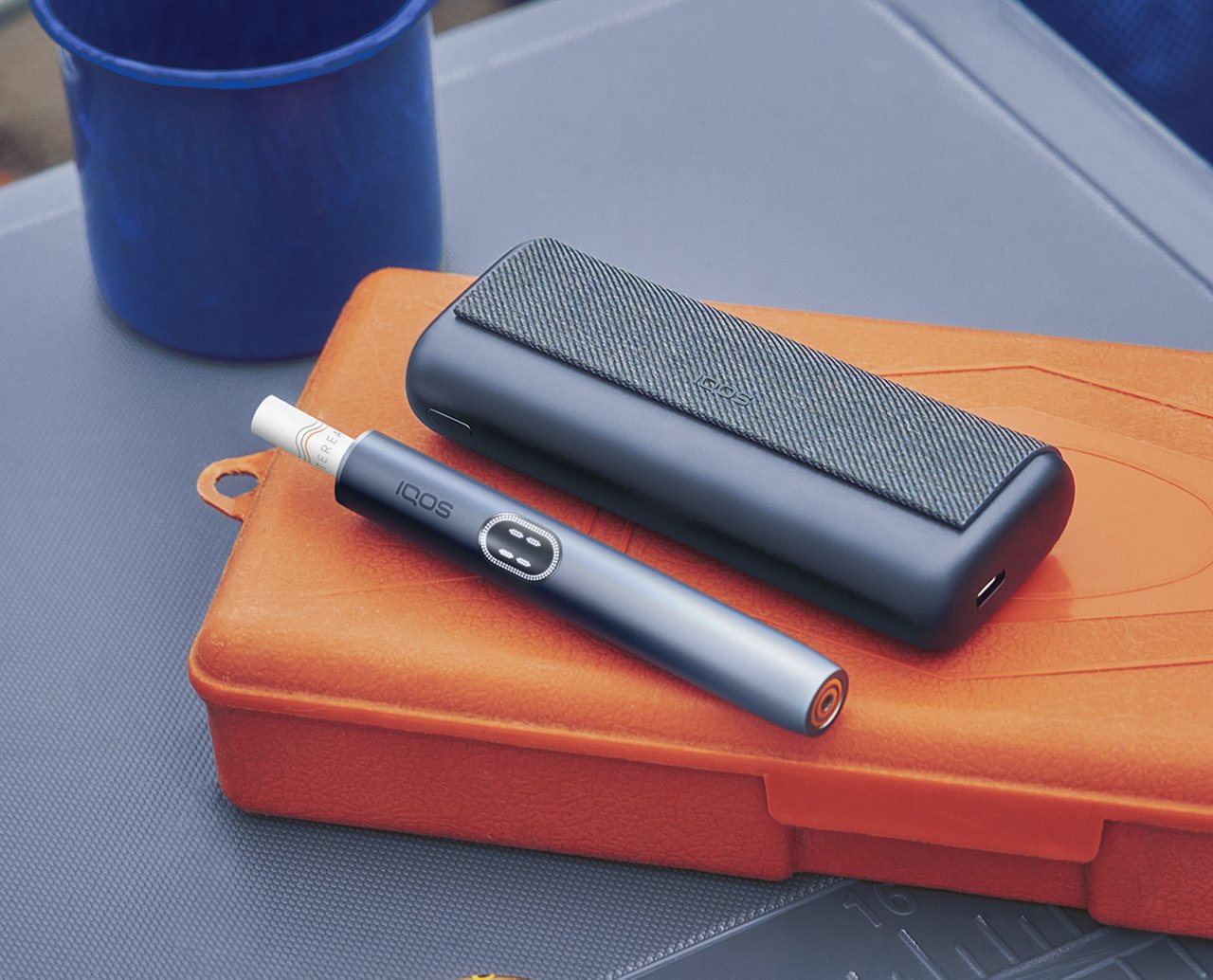 Ein schwarzes IQOS ILUMA PRIME Gerät auf einer orangenen Box